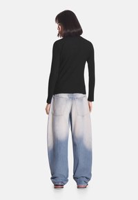 Czarna prążkowana bluzka z długim rękawem połączona z jasnoniebieskimi, oversize dżinsami z efektem wyblakłego gradientu i dwoma tylnymi kieszeniami.