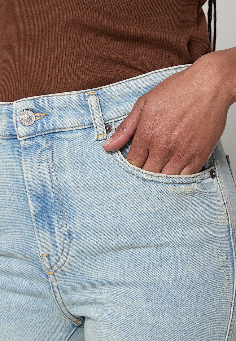 Hellblaue, verwaschene Jeans mit hohem Bund, ausgestattet mit einer Vordertasche, Metallknopfverschluss und sichtbaren Nahtdetails.