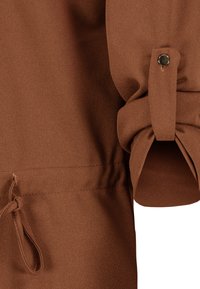 Bruine blouse met een zachte, gladde textuur. HeeftGathered mouwen en een knoopmanchet, met een trekkoorddetail bij de taille.