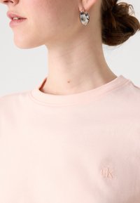 T-shirt in cotone rosa chiaro con scollatura tonda e logo ricamato "ck" sul petto. Texture liscia e morbida con una vestibilità comoda.