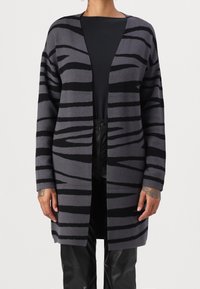Szary i czarny kardigan w paski, otwarty z przodu, z długimi rękawami, o miękkiej fakturze, do połowy długości, noszony na czarnym topie i czarnych spodniach.