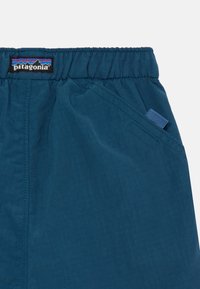 Shorts bleus en tissu léger avec une taille élastique, une poche latérale et une petite étiquette bleue. Présente une texture lisse et un motif en grille subtil.