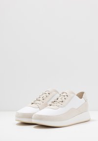 Sneaker con pannelli laterali in pelle bianca, dettagli in suede beige e lacci tondi. Suola spessa bianca che aggiunge altezza. Texture liscia in tutto il corpo.