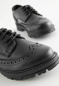 Chaussures en cuir noir avec des pointes arrondies, des détails brogue et des semelles texturées. Elles sont dotées de lacets, d'une finition lisse et d'un design durable.
