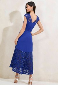 Rochie albastră cu un corset ajustat, mâneci din dantelă și un model floral decupat pe fusta evazată. Spatele are un decolteu în formă de V și închidere cu fermoar.
