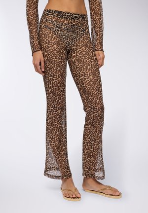 Brązowe spodnie z przezroczystego materiału w lamparcie cętki, z dopasowanym pasem, rozszerzanymi nogawkami i gładką teksturą, noszone z klapkami z akcentami w kolorze złotym.