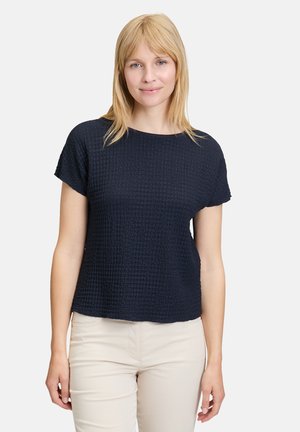 Marineblauw top met korte mouwen en een gestructureerd, wafelachtig patroon. Ronde halslijn, losse pasvorm en een iets gestructureerd ontwerp. Gepaard met lichtgekleurde broek.