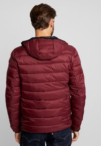 Burgundská péřová bunda s odnímatelnou černou kapucí. Horizontálně prošívaný design, hladká textura a elastické manžety pro těsné přilnutí.