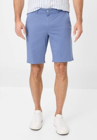 Pantaloni corti in cotone azzurro chiaro con frontale piatto, passanti per cintura e tasche laterali. Abbinati a sneakers bianche e una camicia a righe.