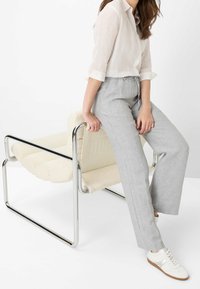 Pantalon en lin gris clair avec taille à cordon de serrage et jambes droites. Associé à une chemise en lin blanche et des baskets blanches. La chaise a un siège rembourré doux crème avec une structure en chrome.