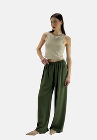 Lichtbeige crop top gecombineerd met loszittende, donkergroene broek. De broek heeft een elastische tailleband; gladde textuur overal.