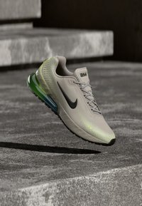 Αθλητικό παπούτσι Nike για τρέξιμο σε ανοιχτό γκρι δίχτυ, με μαύρο σήμα Swoosh, διαφανή πράσινα και μπλε στοιχεία και διακοσμητικές λεπτομέρειες στο πάνω μέρος.
