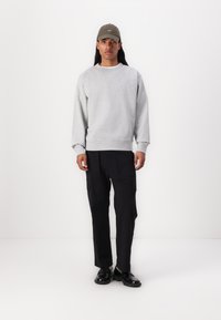 Felpa grigia con polsini a costine, abbinata a pantaloni cargo neri con tasche laterali e scarpe nere. Design minimalista.