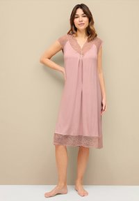 Camicia da notte rosa realizzata in tessuto morbido con bordi in pizzo al colletto e all'orlo. Design senza maniche, leggermente aderente con una silhouette fluida.