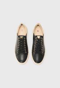 Black leather sneakers with gold eyelets and black laces. Beige rubber sole and cream accents. Smooth texture with minimalistic design.