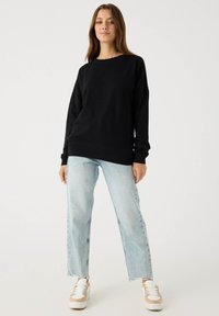 Sudadera negra con cuello redondo y mangas largas, combinada con vaqueros de tiro alto en azul claro y zapatillas de plataforma blancas.