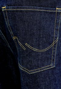 Tmavomodré džínsy z denimu s vreckom a žltým dekoratívnym prešitím na textúre látky, detailný záber.