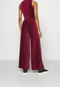 Combinaison large bordeaux en tissu doux, dotée d'un design sans manches, d'une taille élastique, et associée à des baskets noires.