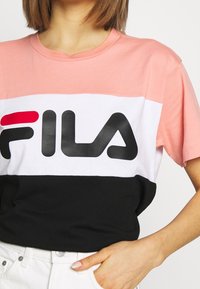 Färgblockerad T-shirt med ljusrosa, vit och svarta sektioner. Svart "FILA"-logotyp tryckt framträdande på bröstet. Tillverkad av bomull.