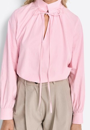 Light pink long-sleeve blouse with vertical white stripes, high collar, keyhole neckline, and tie detail. Worn with beige high-waisted trousers.
