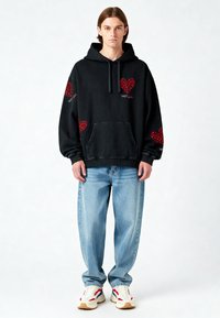 Melna kapucēta džemperis ar sarkanu sirds rakstu, ar priekšējo kabatu, brīva piegriezuma. Kombinēts ar gaiši ziliem platām biksēm un baltām kedām ar sarkanām akcentiem.