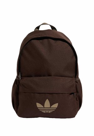Brun rygsæk med frontlynlåslomme og beige Adidas trefoil-logo centreret på lommen, stofhåndtag øverst.