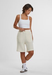 Hvit avskåret tank topp parret med lyse beige strikkede shorts. Shortsene har et teksturert mønster og rullede kanter. Uformelt fottøy fullfører antrekket.