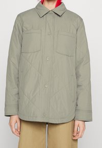 Ljust grön, vadderad jacka med knappfront, spridd krage och två bröstfickor. Har en slät yta och rundad nederkant.