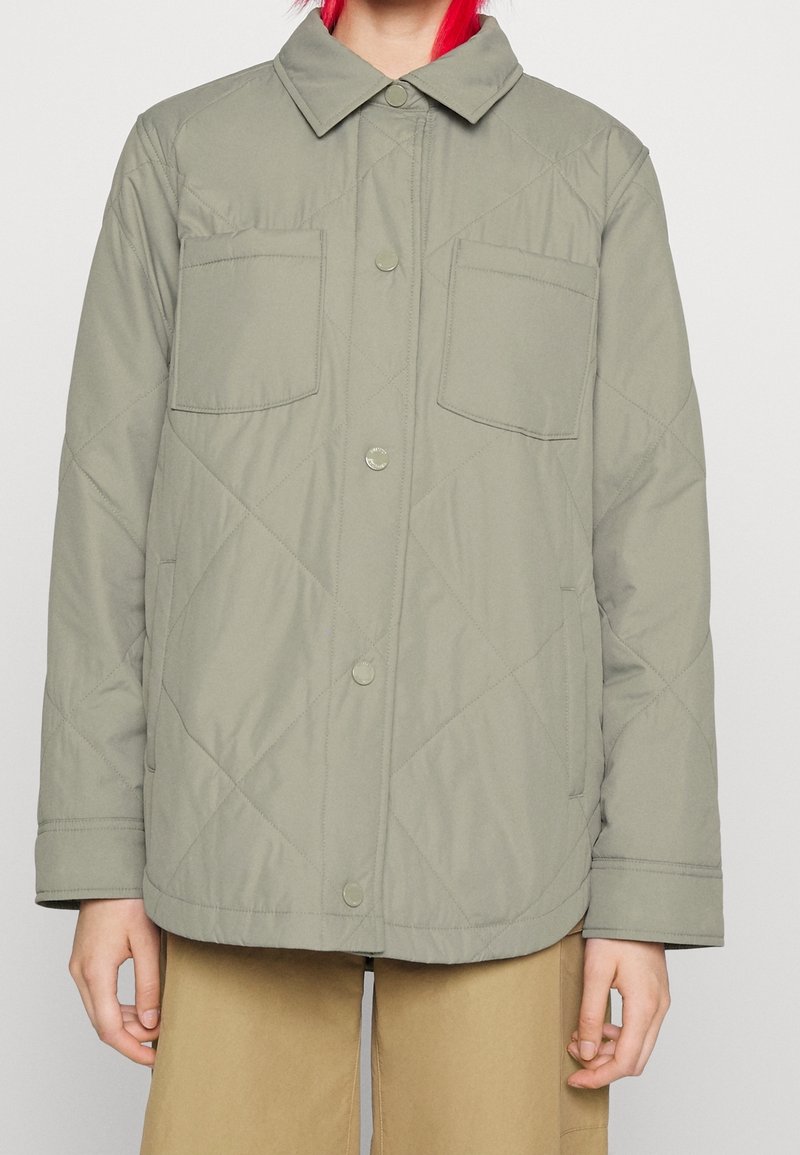 Ljust grön, vadderad jacka med knappfront, spridd krage och två bröstfickor. Har en slät yta och rundad nederkant.