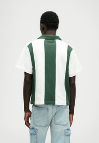 Groene en witte gestreepte polo met kraag, korte mouwen en een relaxte pasvorm; gemaakt van zachte stof met een gladde textuur.