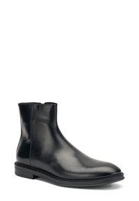 Botín de cuero negro hasta el tobillo con un acabado suave, punta redonda y un diseño minimalista. Presenta una cremallera lateral y una suela de perfil bajo.