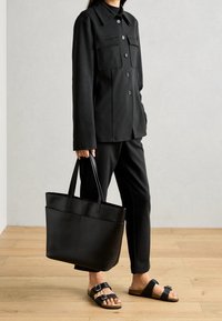 Czarna dopasowana marynarka z przodu na guziki, dopasowane spodnie, czarna torba na ramię i sandały z dwoma regulowanymi paskami. Gładka tkanina i elegancki design.