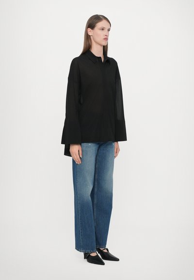 Zwarte langemouw shirt met een puntkraag, gecombineerd met losse blauwe spijkerbroeken en zwarte puntige schoenen. Eenvoudig en modern ontwerp.