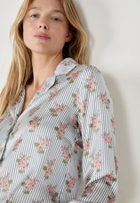 Blusa con estampado de flores y rayas verticales en azul y blanco, que presenta un cuello tipo camisero y un tejido suave y ligero.