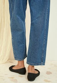 Donkerzwarte balletflats met een ronde neus en een gestructureerde bovenkant, gecombineerd met brede blauwe denimbroeken met een rafelige zoom en lichte stiksels.