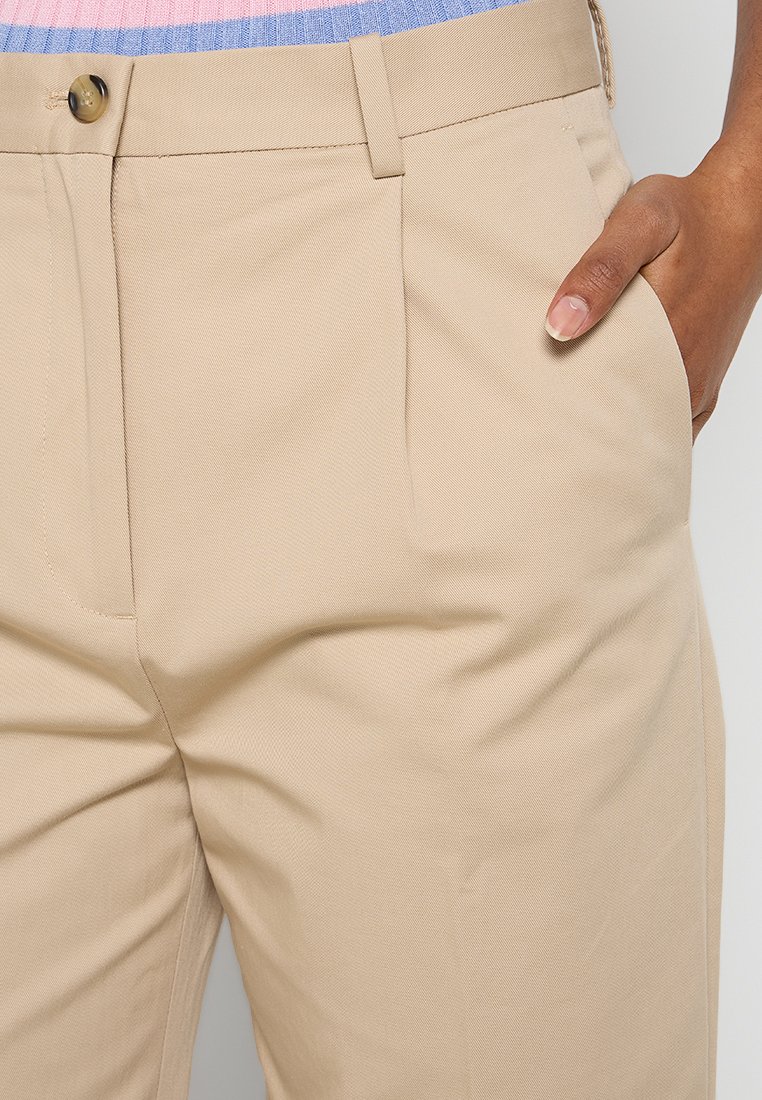 Pantaloni beige su misura con una texture liscia, dotati di tasche laterali e chiusura con un singolo bottone in vita.