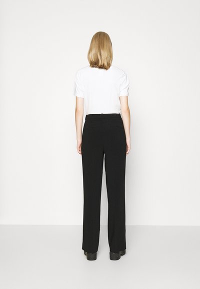 Zwarte, wijde broek van soepel materiaal, met een aansluitende taille en achterzakken, gecombineerd met een eenvoudige witte shirt met korte mouwen.