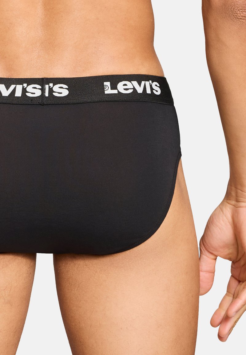 Männlicher Oberkörper und Hand, die schwarze Levi's-Slips mit sichtbarem markiertem Bund tragen, von hinten vor weißem Hintergrund gezeigt.