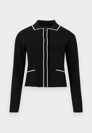 Zwarte cardigan met een kraag en crèmekleurige piping langs de kraag en zakken, en zes knopen aan de voorkant. Heeft lange mouwen en een cropped ontwerp.