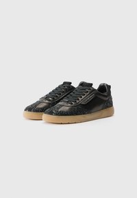 Baskets noires avec une tige en cuir glossy, des accents scintillants et une semelle en caoutchouc gomme. Design à lacets avec une forme angulaire distincte.