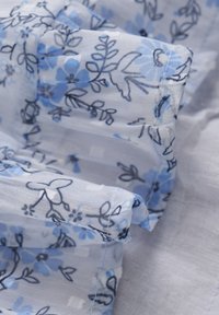 Lätt, genomskinlig tyg med vit bakgrund och blå blommönster. Har intrikata detaljer i mörkblå konturer och en mjuk textur.