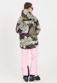 Mehrfarbige outerwear Jacke mit wirbelnden Mustern in Grün und Braun, kombiniert mit hellrosa Hosen und schwarzen Schneestiefeln.