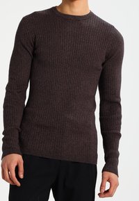Pull marron foncé côtelé avec manches longues, encolure ronde et coupe ajustée. La texture tricotée améliore la chaleur et le confort.