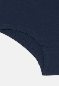 Tissu bleu marine avec des coutures incurvées et un piquage texturé sur le bord d'un vêtement, montrant des finitions et des constructions de coutures détaillées.