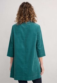 Veste en velours côtelé turquoise à manches trois-quarts, coupe droite et détails de couture subtils. Texture lisse et longueur mi-mollet.