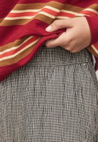 Red striped sweater with a soft texture, layered over a black and white checkered skirt featuring pleats and an elastic waistband.