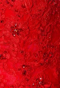 Röd broderad tyg med blommönster, prydd med pärlor och paljetter, som uppvisar en texturerad, rik yta.