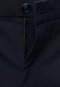 Granatowe materiałowe spodnie z widocznym zapięciem na zamek, guzikiem z czaszką oraz czystym, teksturowanym wykończeniem.