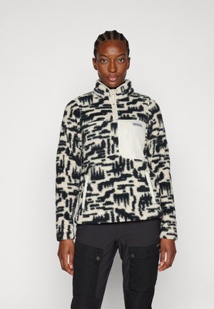 Fleece pullover in crème en marineprint, met een ritskraag, een witte borstzak en een gestructureerde stof. Zwarte cargobroek wordt daaronder gedragen.