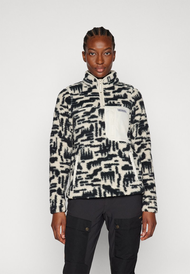 Pullover in pile con stampa crema e blu navy, dotato di collo a zip, tasca sul petto bianca e tessuto strutturato. Sotto sono indossati pantaloni cargo neri.